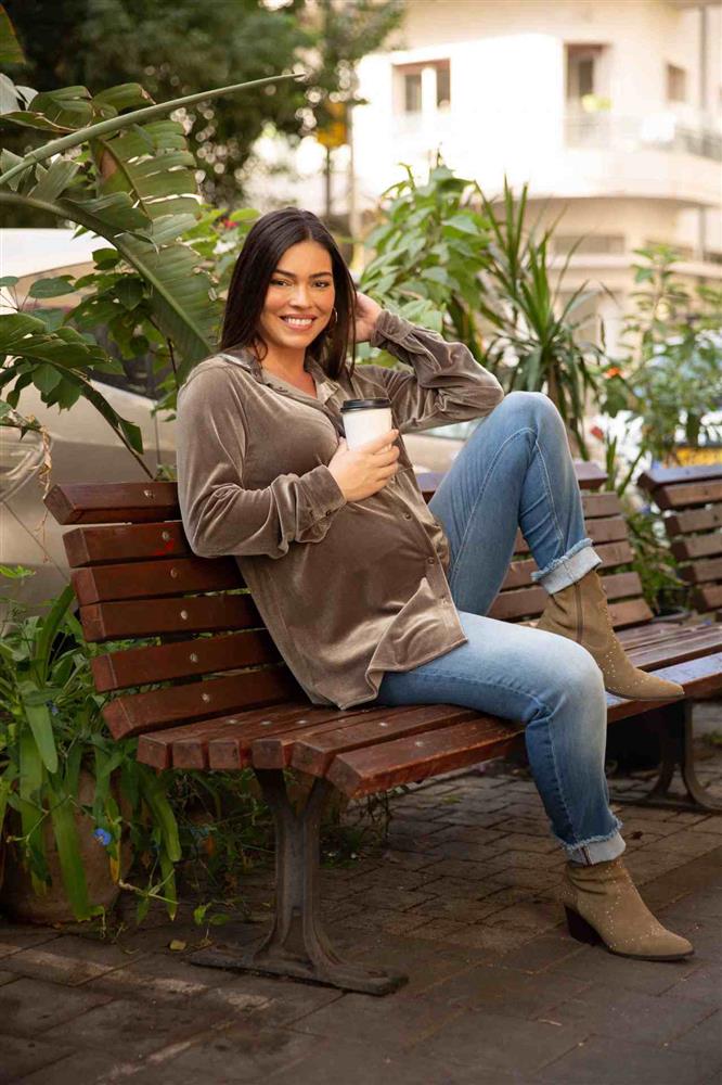 A woman sits comfortably on a bench wearing maternity jeans
